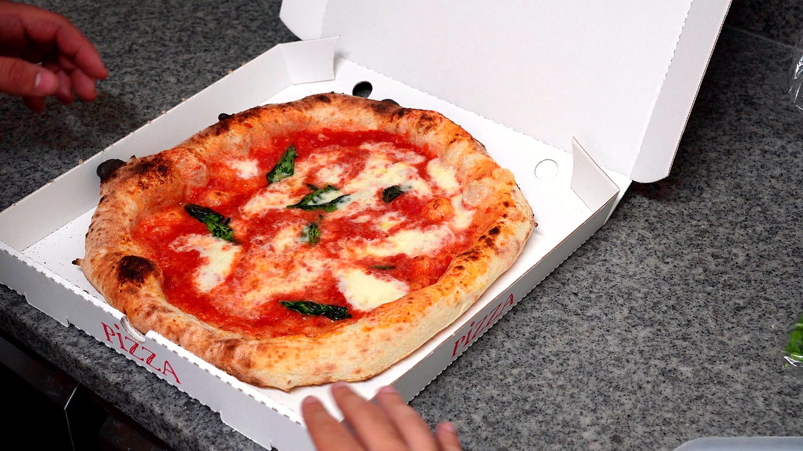 Frisch gebackene Margherita im Karton, Hände am Rand