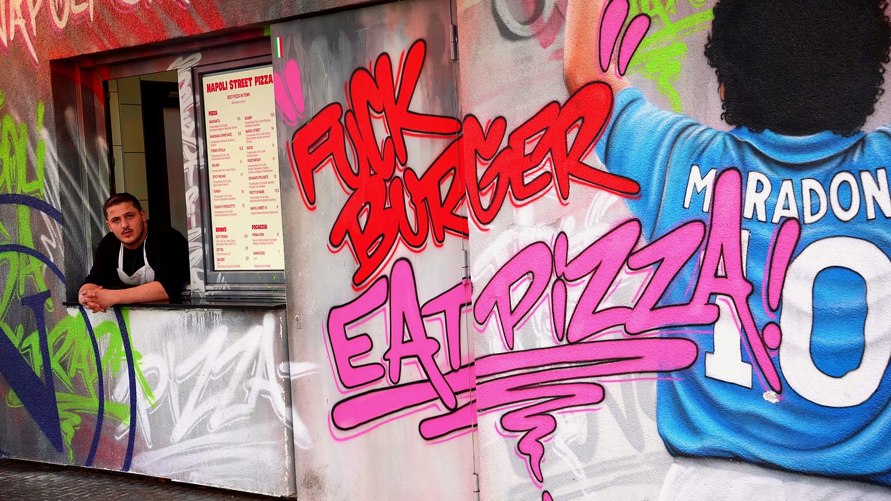 Die gesprühte Wand am Laden: FUCK BURGER EAT PIZZA neben Maradona im Napoli-Trikot mit der 10